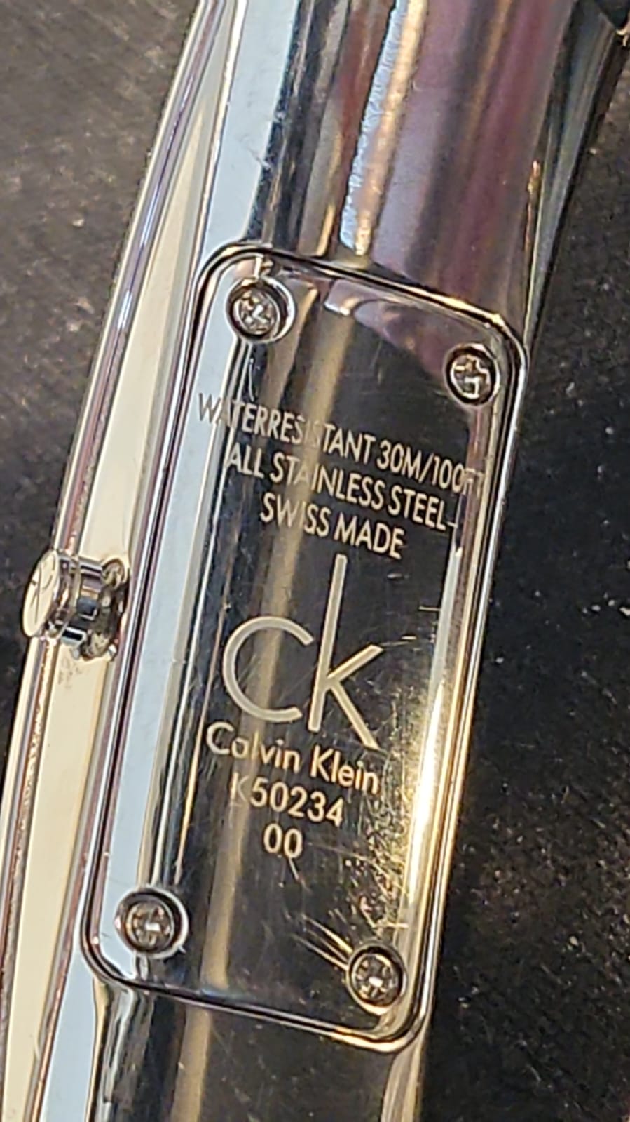 Close-up of the engraved case back showing 'Water Resistant 30M/100FT', 'All Stainless Steel', 'Swiss Made', 'ck Calvin Klein', and model number K50234.