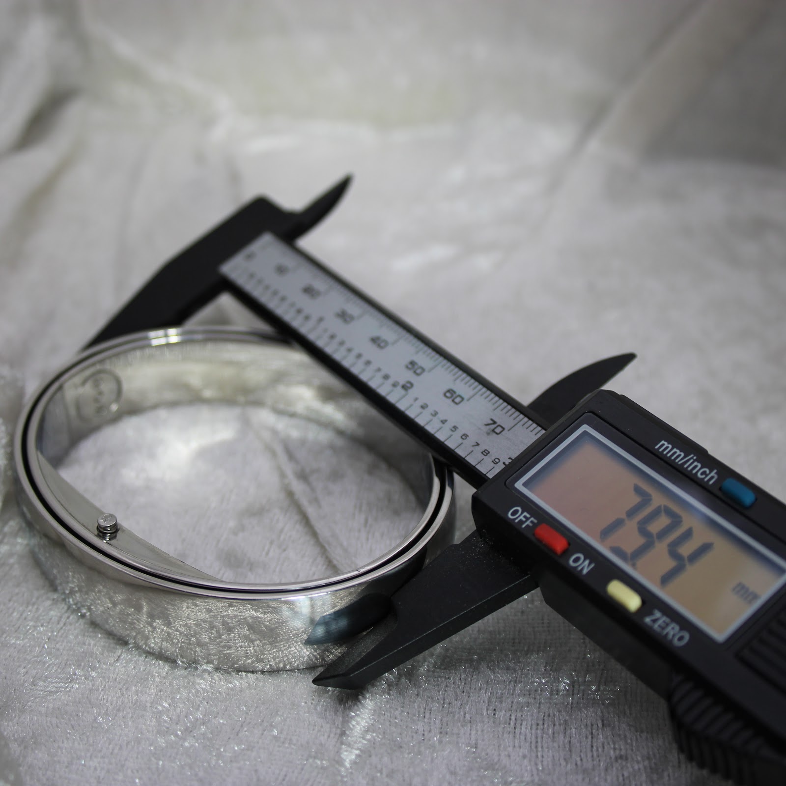Digital caliper measuring the outer width of the integrated stainless steel bangle bracelet, showing 79.4 mm.