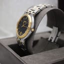 Angled side view of the Gucci 9000G watch on a grey display cushion, highlighting the case profile, gold crown, and two-tone bracelet.