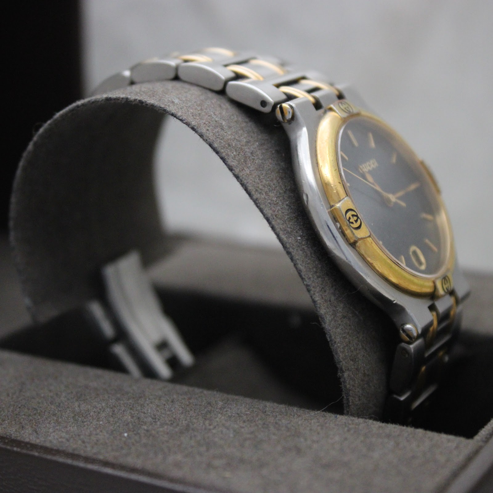 Another angled side view of the Gucci 9000G watch on a grey display cushion, focusing on the bracelet and case side.