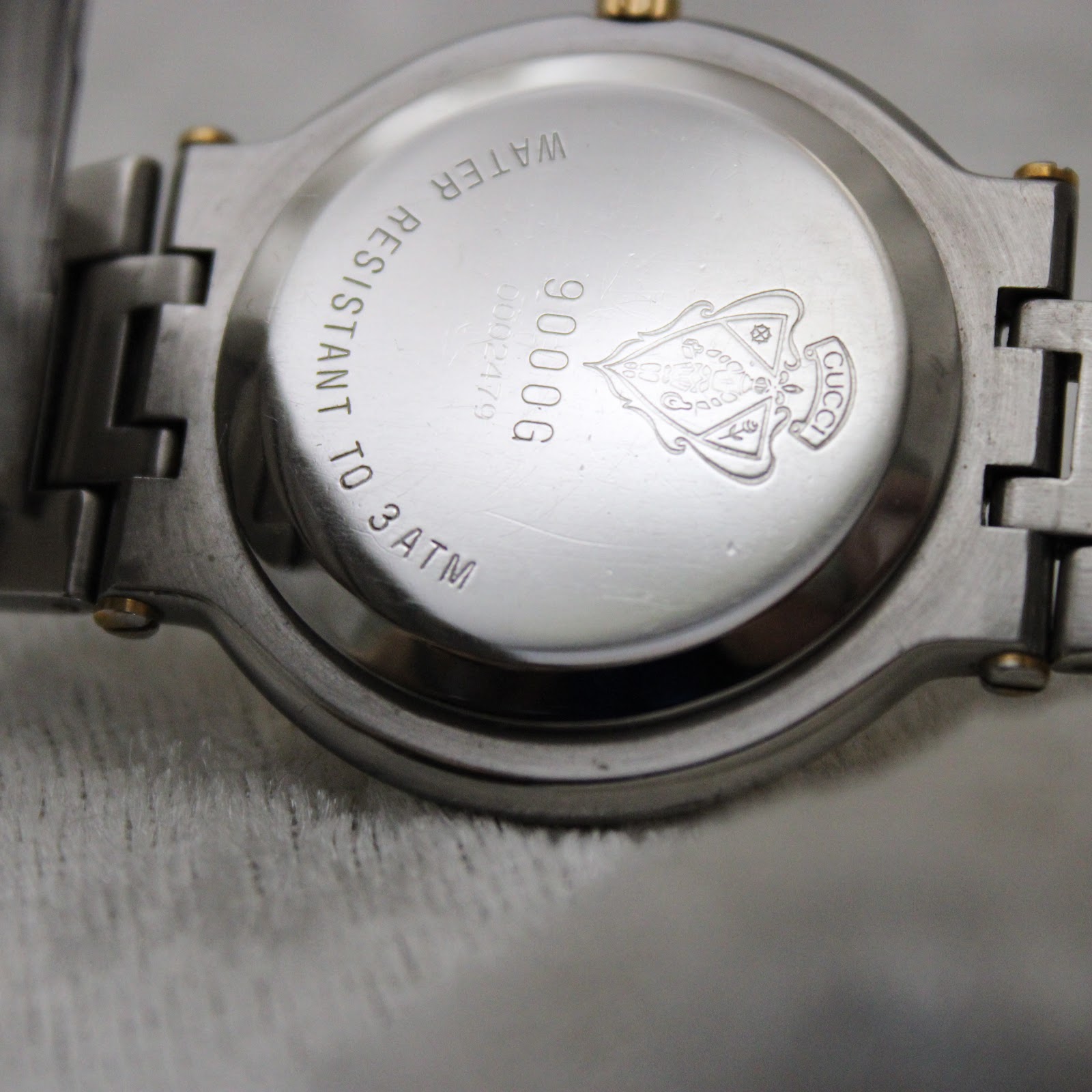 Close-up of the polished stainless steel case back of the Gucci 9000G, with 'water resistant to 3 atm', '9000G', serial number, and Gucci crest engraving.