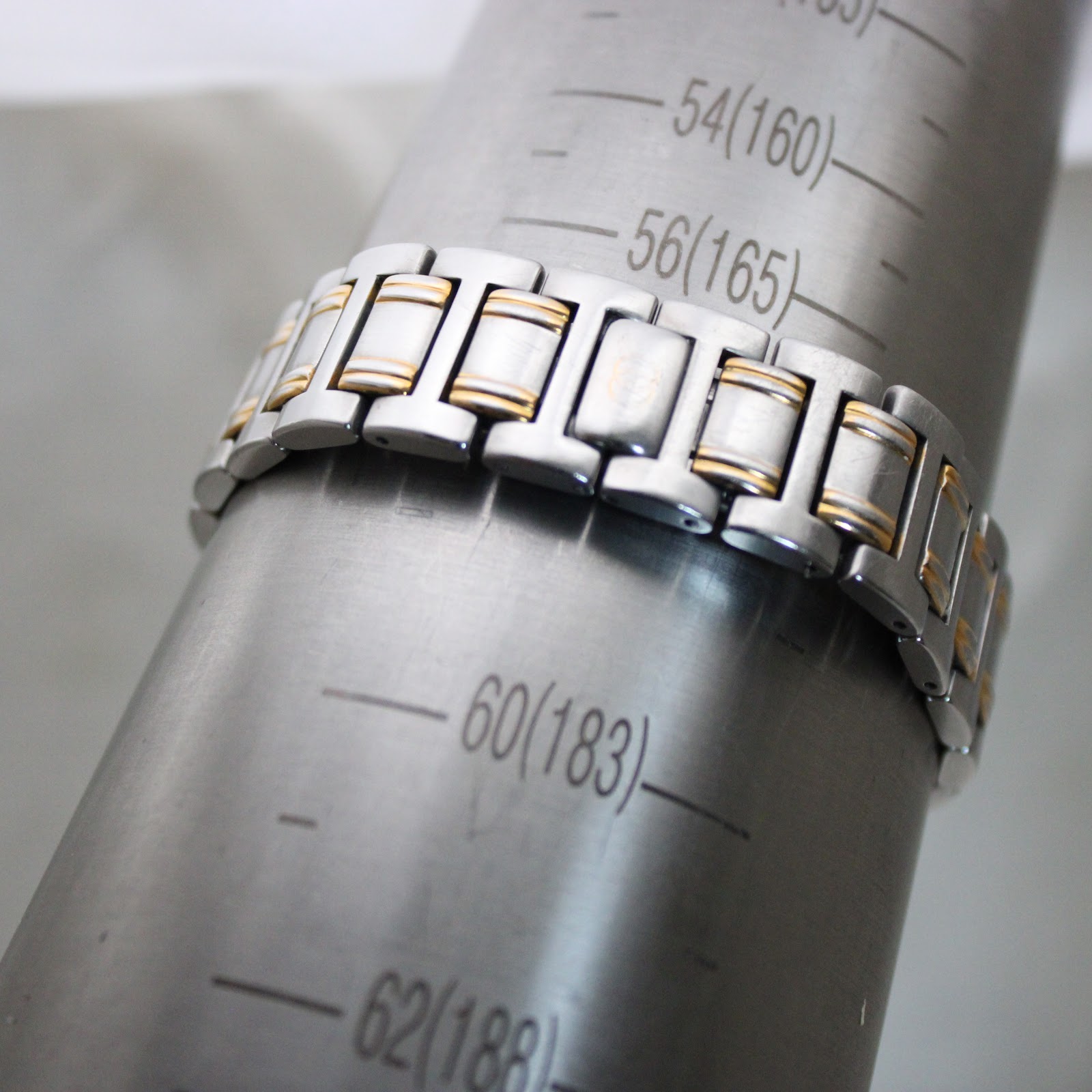 The two-tone bracelet of the Gucci 9000G on a wrist sizing gauge, indicating a wrist circumference of '183mm' (60).