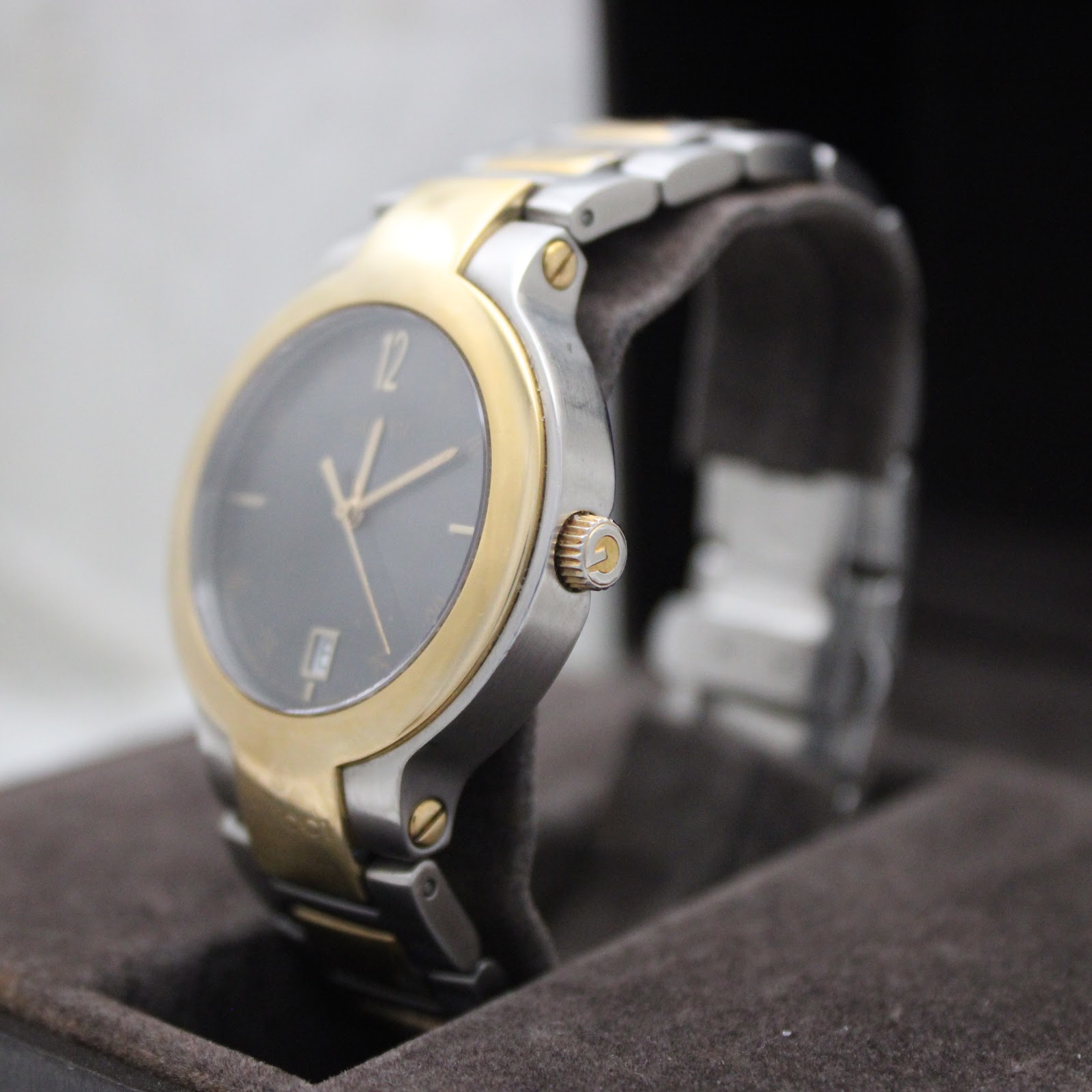 Angled side view of the Gucci 8900M watch, highlighting the gold-tone crown and two-tone bracelet, in its box.