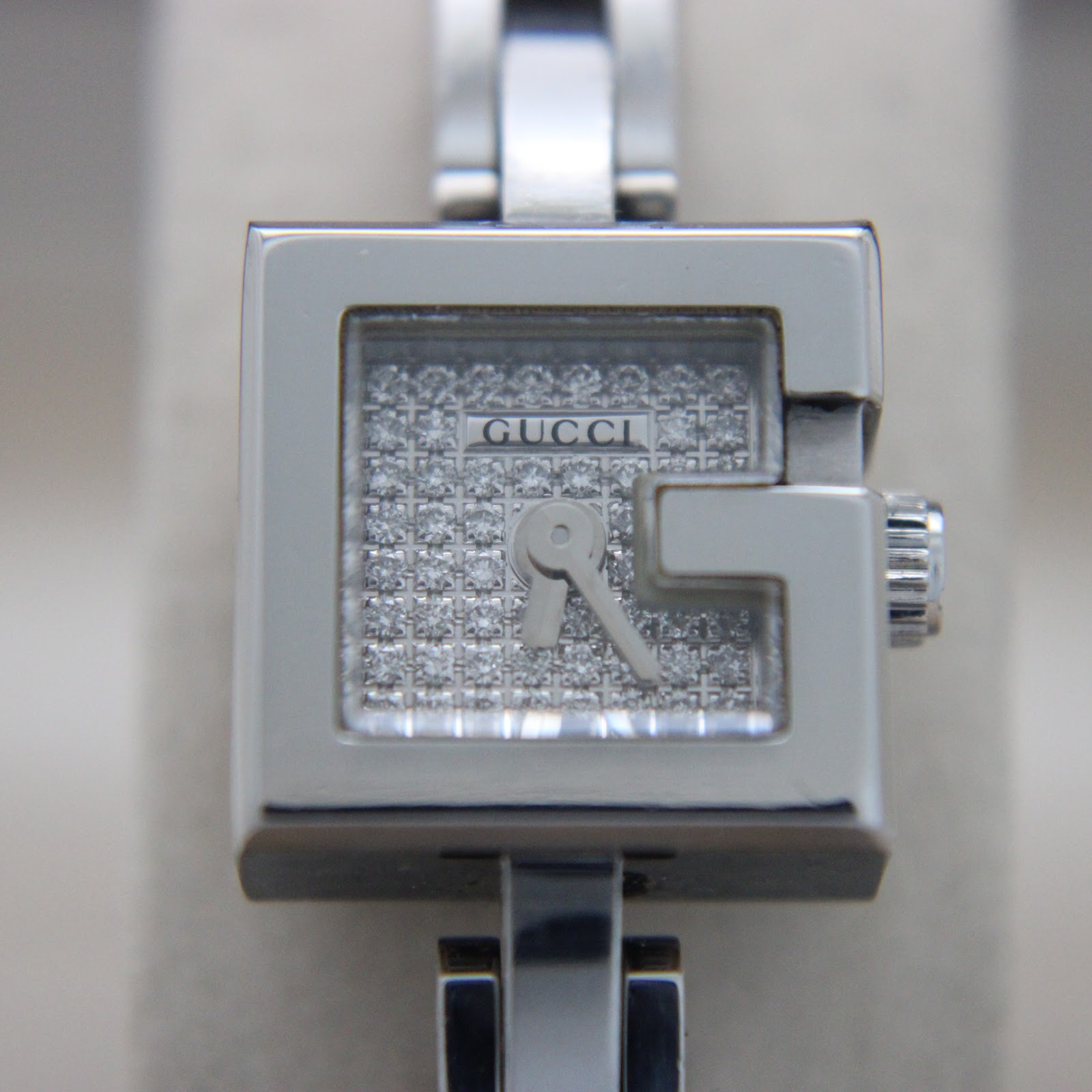 Close-up front view of the Gucci 102 G-frame watch dial, showing 'G' shaped bezel and textured silver face.