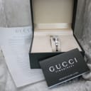 Overhead view of the Gucci 102 G-frame watch in its original box, alongside the warranty card and booklet.