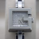 Close-up front view of the Gucci 102 G-frame watch dial, showing 'G' shaped bezel and textured silver face.