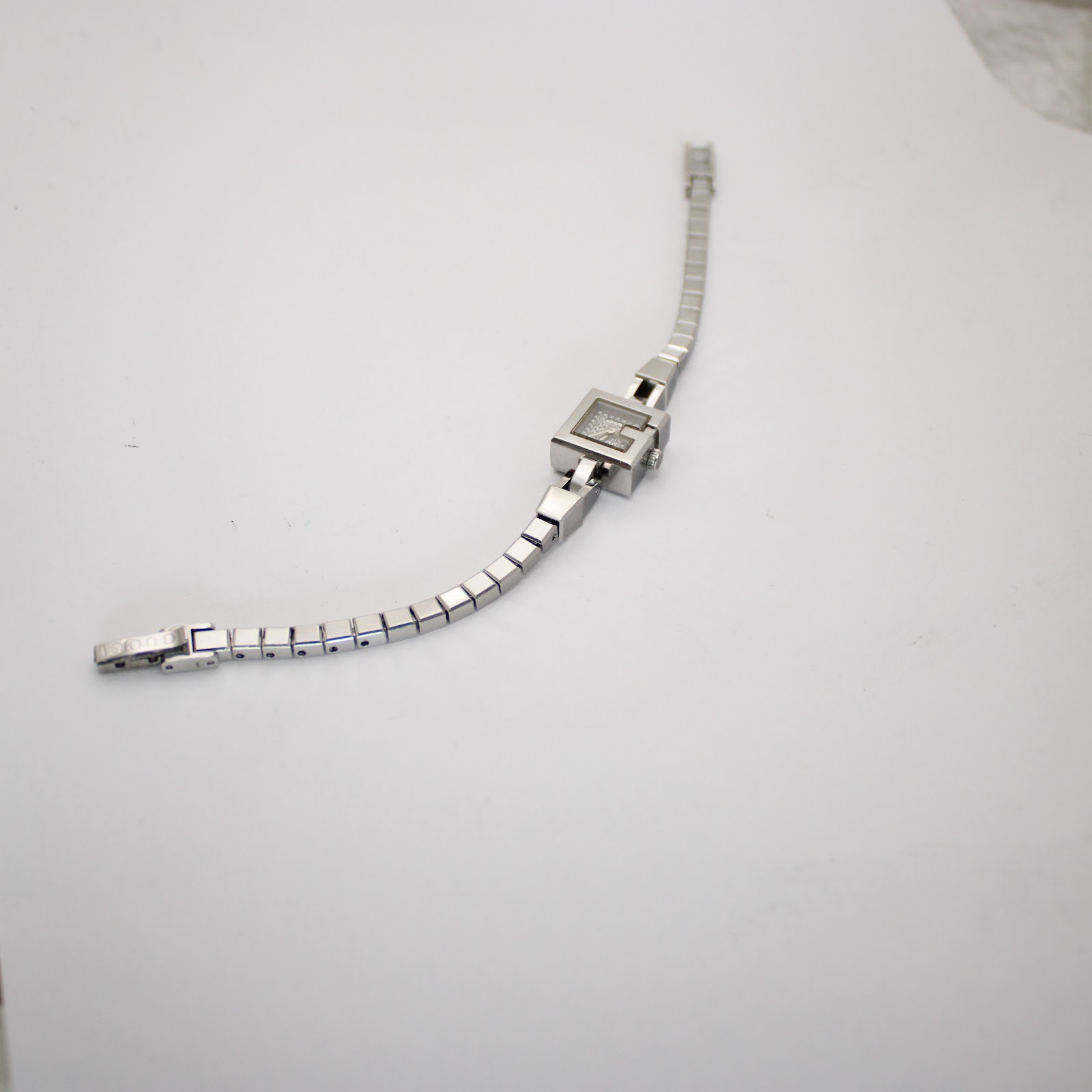 Full overhead view of the Gucci 102 G-frame watch with its stainless steel bracelet extended on a white background.