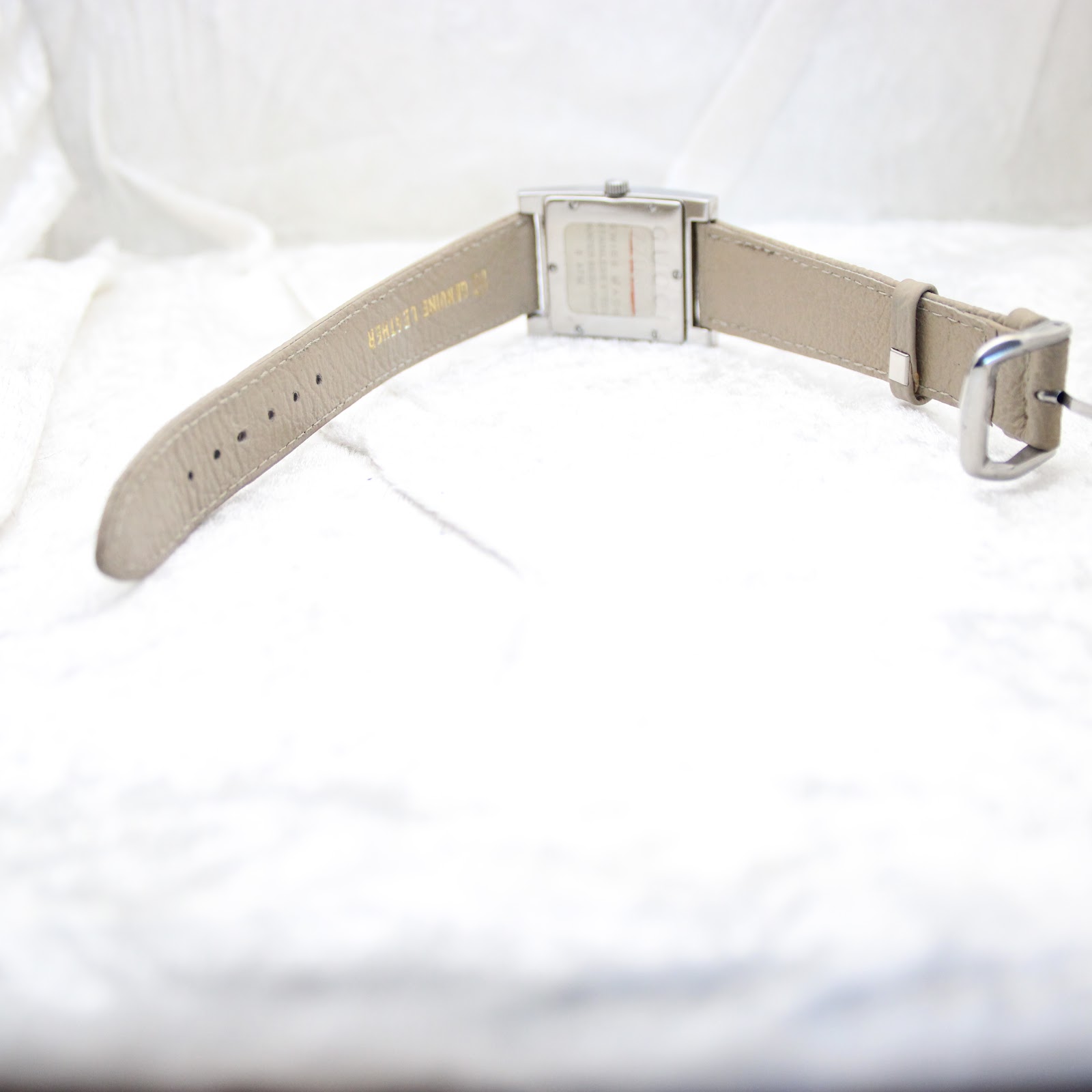View from behind the watch showing the full length of the beige leather strap and its stainless steel buckle.