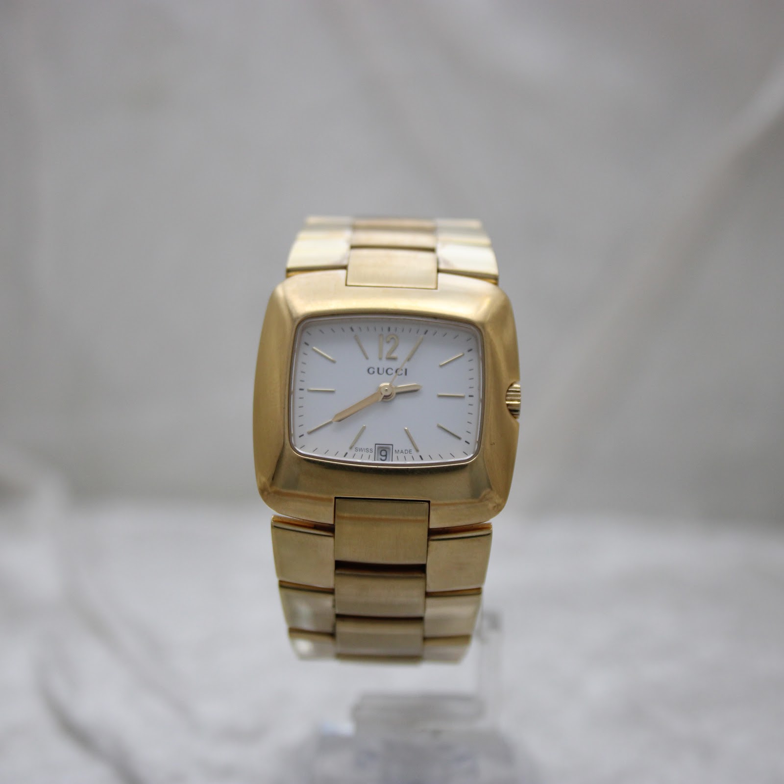 Full front view of the gold-tone Gucci 8500L watch on a clear stand, highlighting its integrated bracelet.
