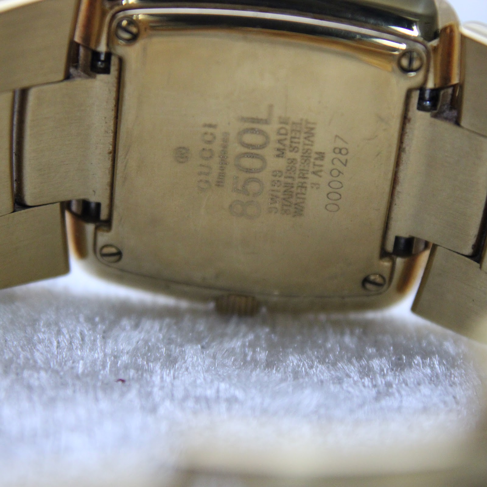 Close-up of the gold-tone case back showing 'Gucci', '8500L', 'Swiss Made', 'Stainless Steel', 'Water Resistant 3 ATM', and serial number '0009287'.