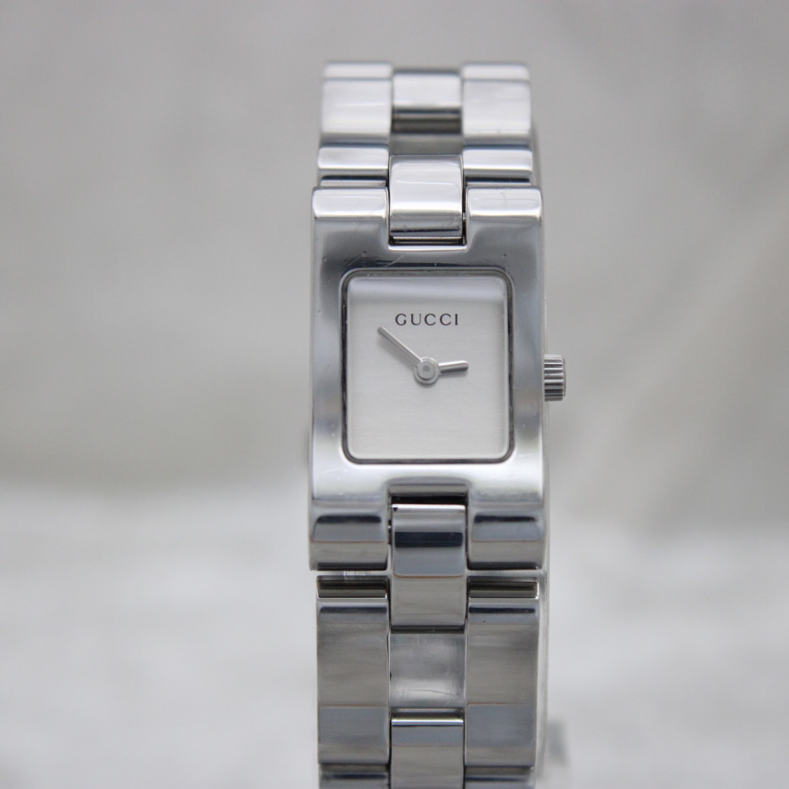 Slightly closer front view of the Gucci 2305L watch, highlighting the brushed silver dial, 'GUCCI' logo, and polished stainless steel case and bracelet links.