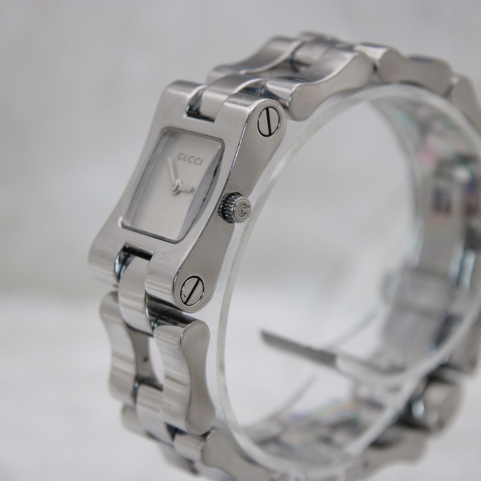 Angled side view of the Gucci 2305L watch on a clear stand, showing the watch case, integrated bracelet design, and the crown with 'G' logo.