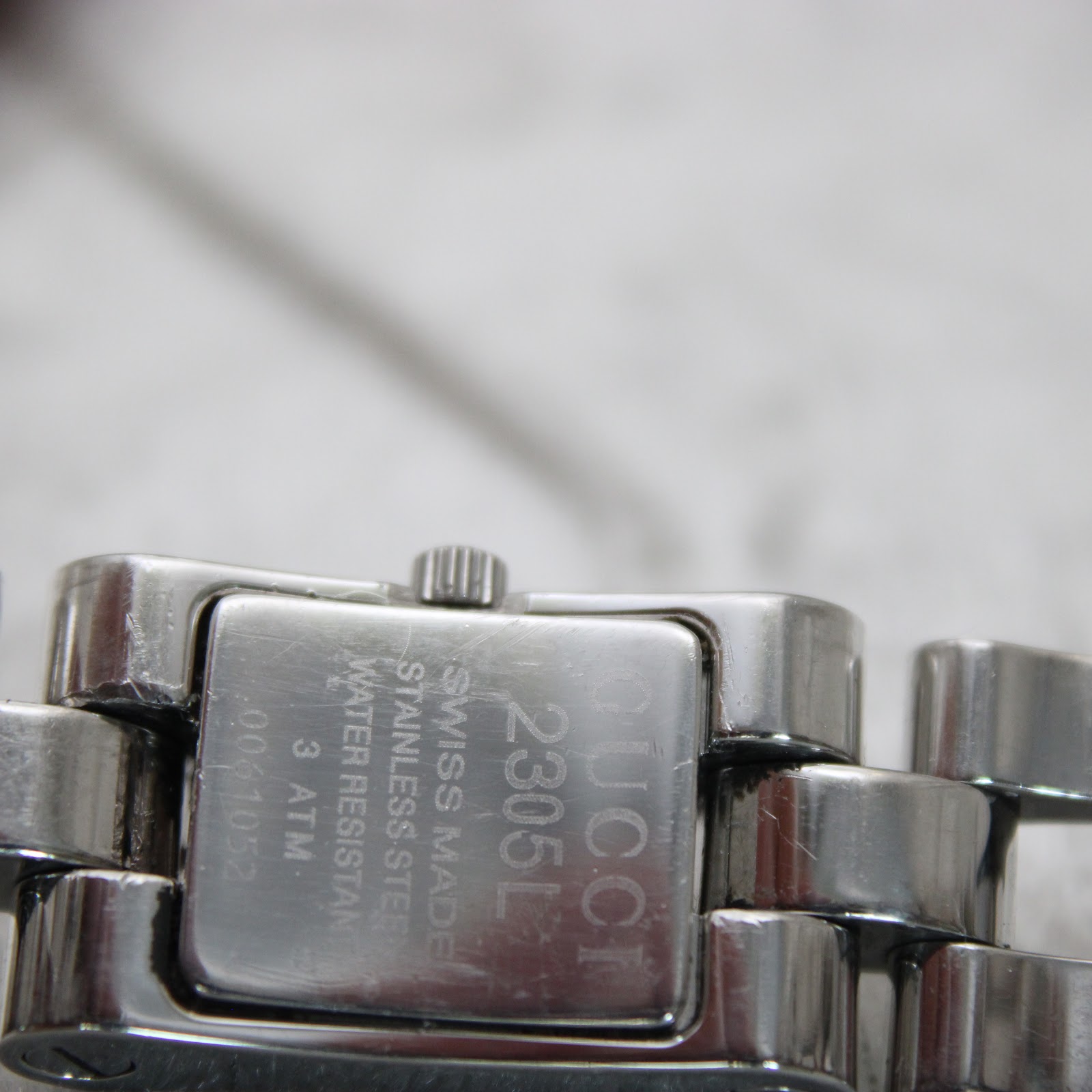 Close-up of the watch case back, showing 'GUCCI 2305L', 'SWISS MADE', 'STAINLESS STEEL', 'WATER RESISTANT 3 ATM', and serial number '0061052'.