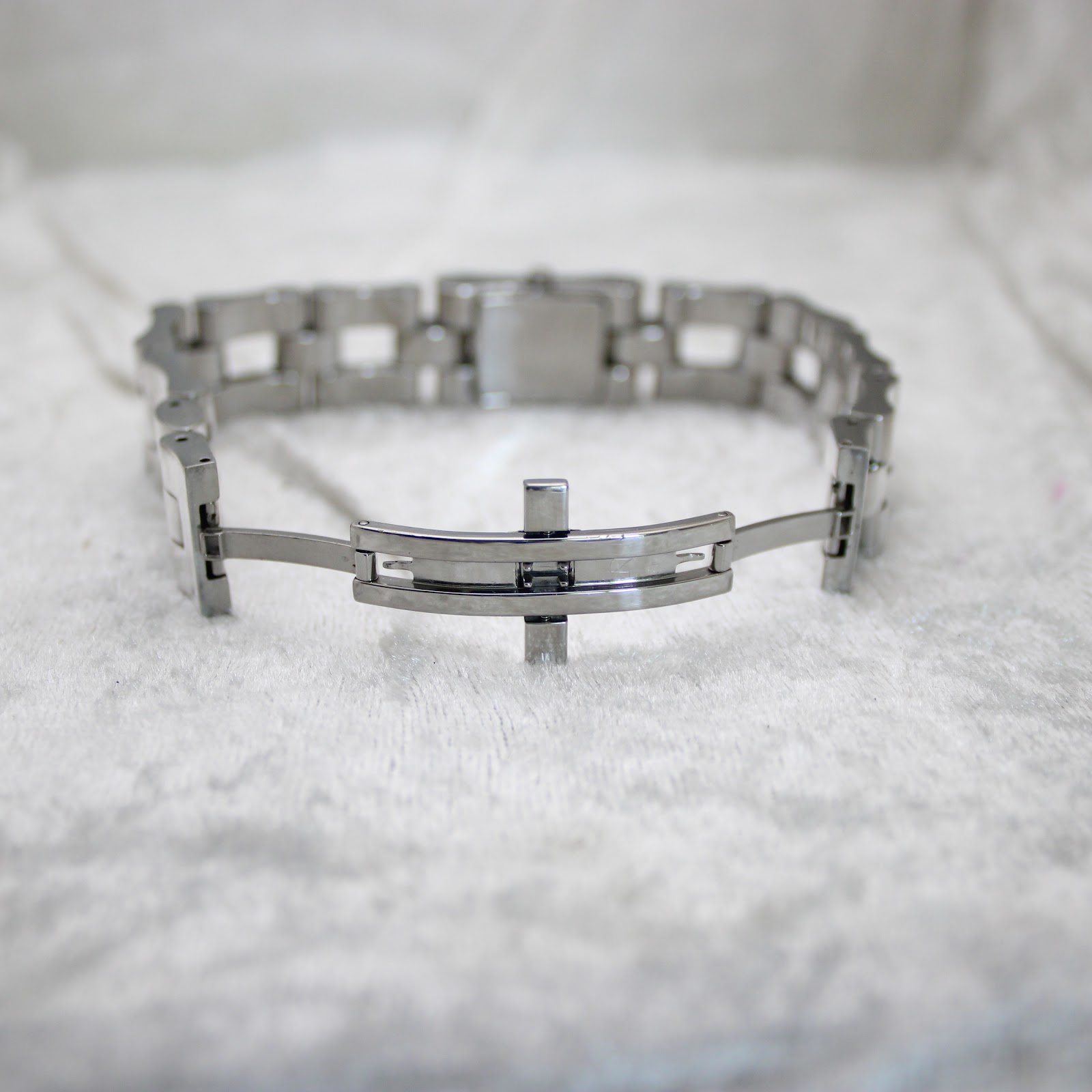 Interior view of the stainless steel bracelet, showing the hidden deployant clasp mechanism open on a white textured surface.