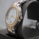 Angled side view of the Gucci 8900M watch, highlighting the gold-tone crown and the brushed stainless steel case on a grey display cushion.