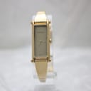 Front view of the Gucci 1500L watch on a stand, showing the rectangular gold-tone case, minimalist champagne dial, and integrated bangle.