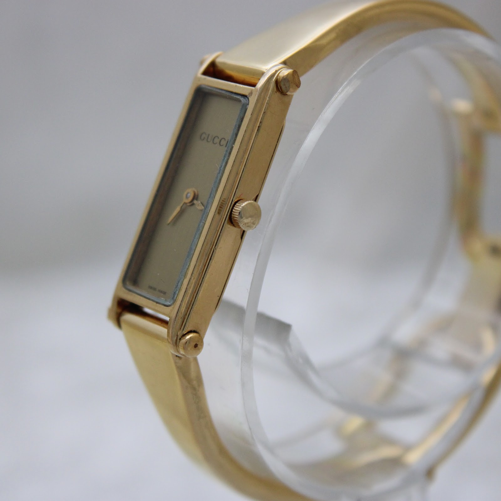 Angled view of the Gucci 1500L watch, highlighting the gold-tone case, crown, and the seamless design of the bangle.