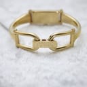 View of the open gold-tone bangle clasp, with "GUCCI" engraved on the fold-over component, resting on a white textured surface.