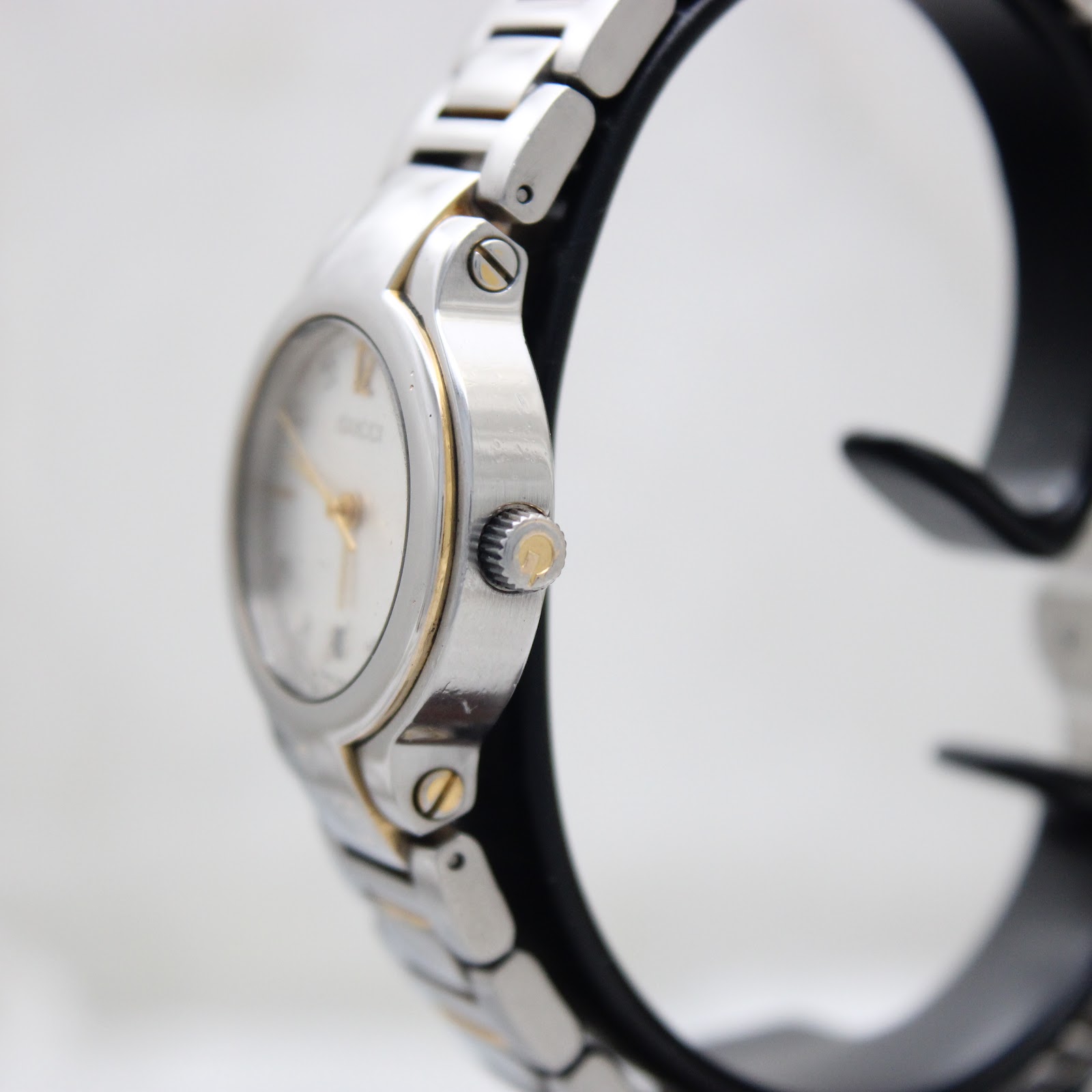 Side profile of the Gucci 8900L watch, highlighting the signed crown and two-tone case details on a watch stand.