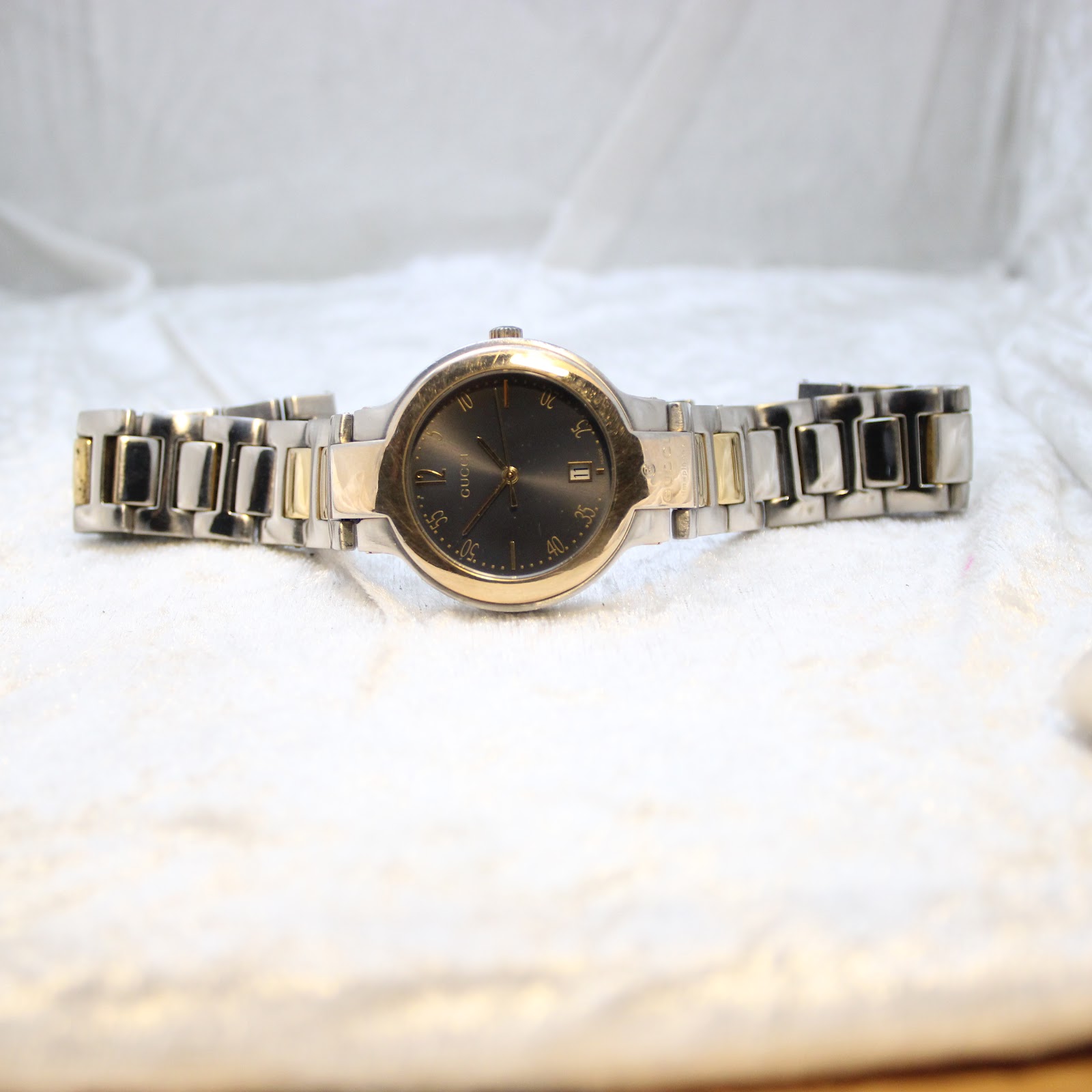 Full length view of the Gucci 8900M watch laid flat on a white textured surface, showcasing the entire two-tone bracelet.