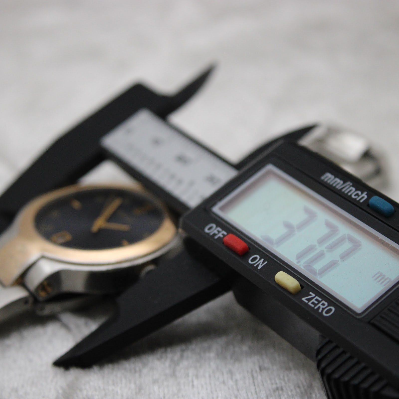 Digital caliper displaying 37.70 mm, measuring the case diameter of the Gucci 8900M watch.