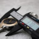 Digital caliper displaying 37.70 mm, measuring the case diameter of the Gucci 8900M watch.