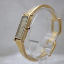 Angled view of the gold-tone Gucci 1500L watch, showing the side of the rectangular case, crown with blue cabochon, and bangle bracelet.