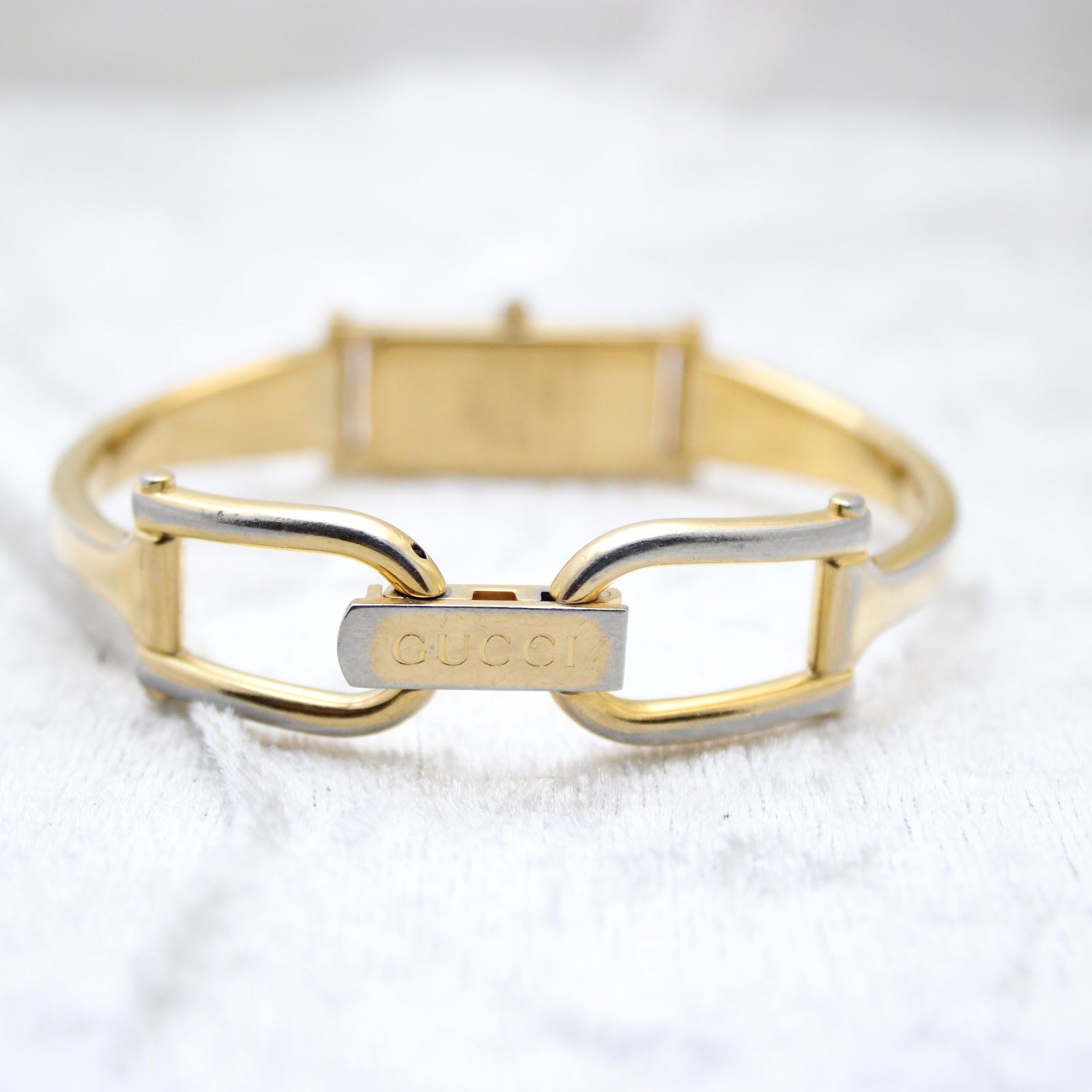 Close-up of the engraved Gucci fold-over clasp on the gold-tone bangle bracelet, showing some plating wear.