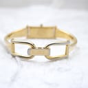 Close-up of the engraved Gucci fold-over clasp on the gold-tone bangle bracelet, showing some plating wear.