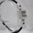 Side-angled view of the Gucci 102 watch on a clear stand, showing the minimalist black dial and the design of the stainless steel links.