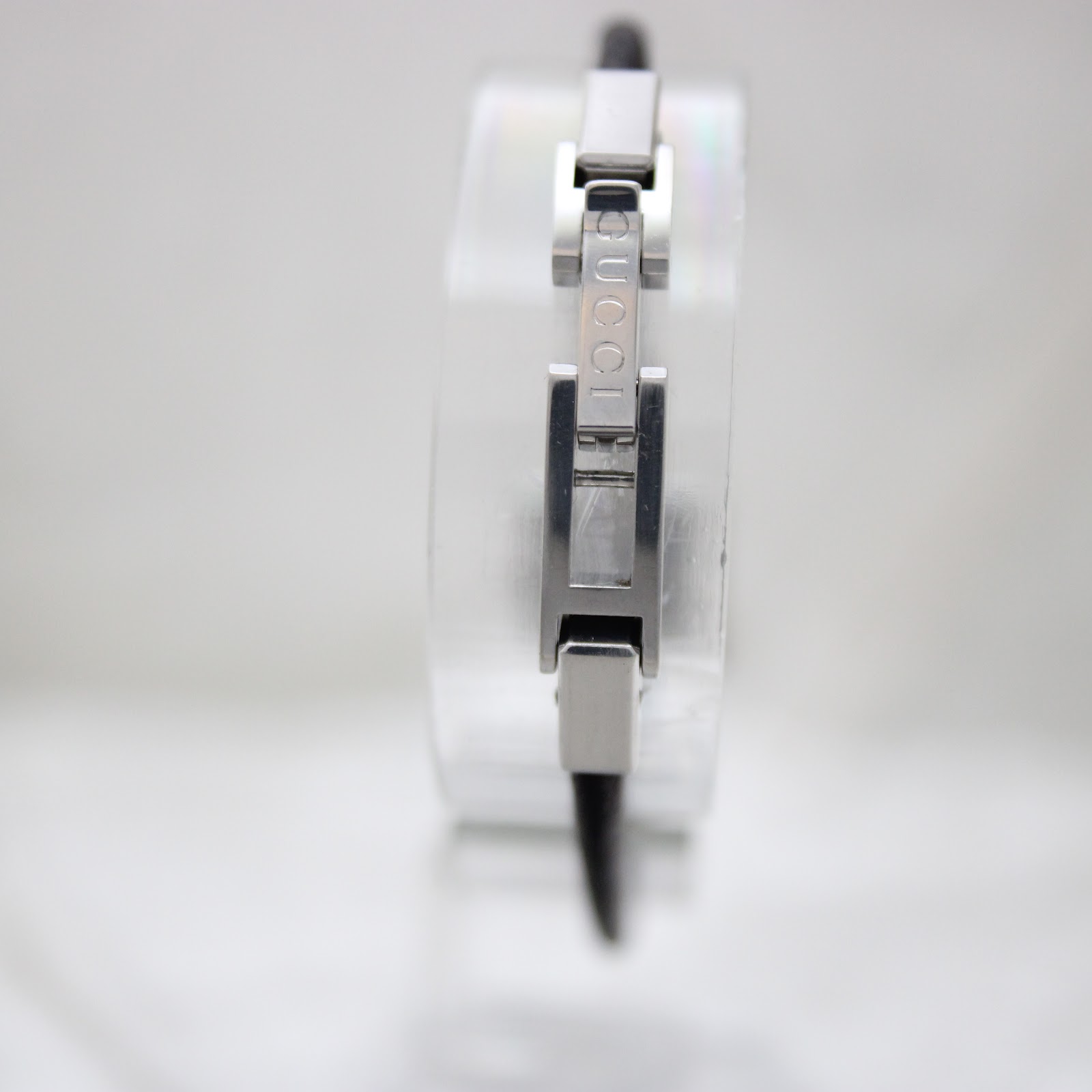 View of the watch's clasp, showing the 'GUCCI' engraving on the stainless steel link, part of the black leather cord strap.