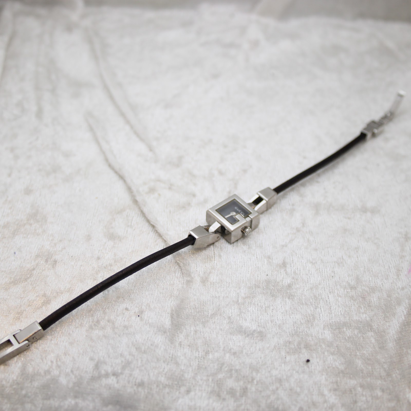 Overhead angled view of the Gucci 102 watch, showcasing the full length of the black leather cord strap and silver-tone links.