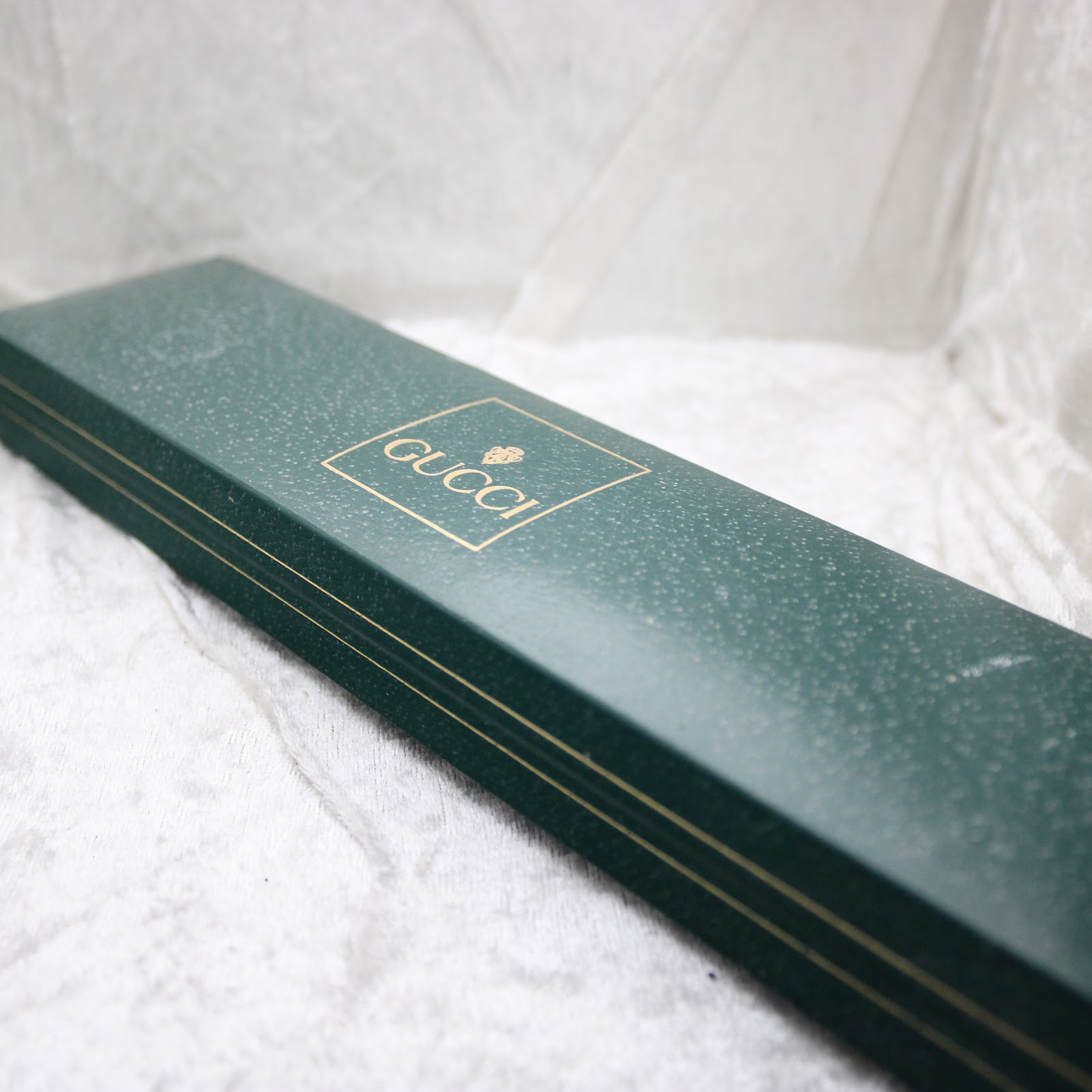 Top-down view of the original green Gucci watch box with the gold embossed 'GUCCI' logo and brand symbol.