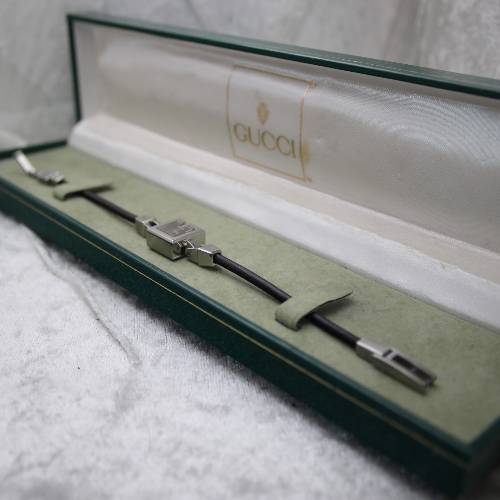 The Gucci 102 watch resting inside its opened original green Gucci box, which has a cream fabric interior.