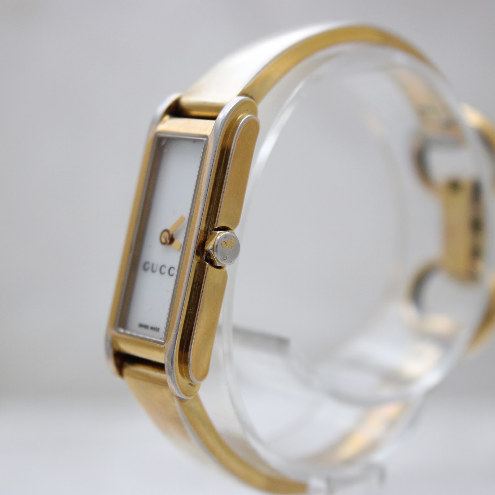 Angled view of the Gucci 109 watch, showing the gold-tone crown and the two-tone bangle bracelet.