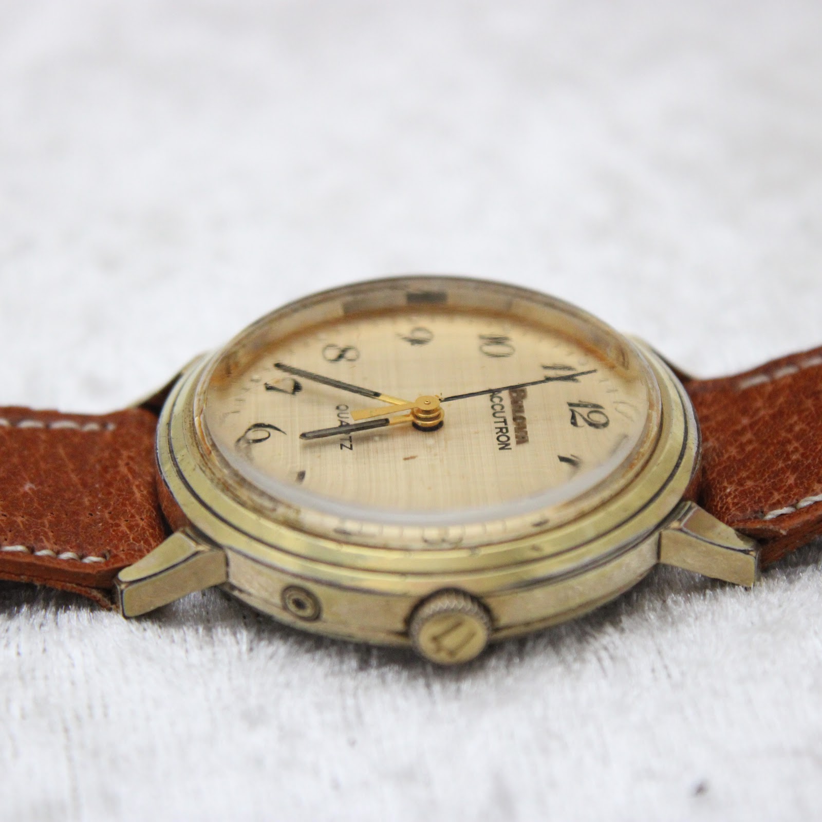 Close-up side view of the watch case and crown on a white surface, showing wear on the gold plating.