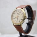 Angled side view of the Bulova Accutron watch on a display stand, showing the gold-plated case and brown leather strap.