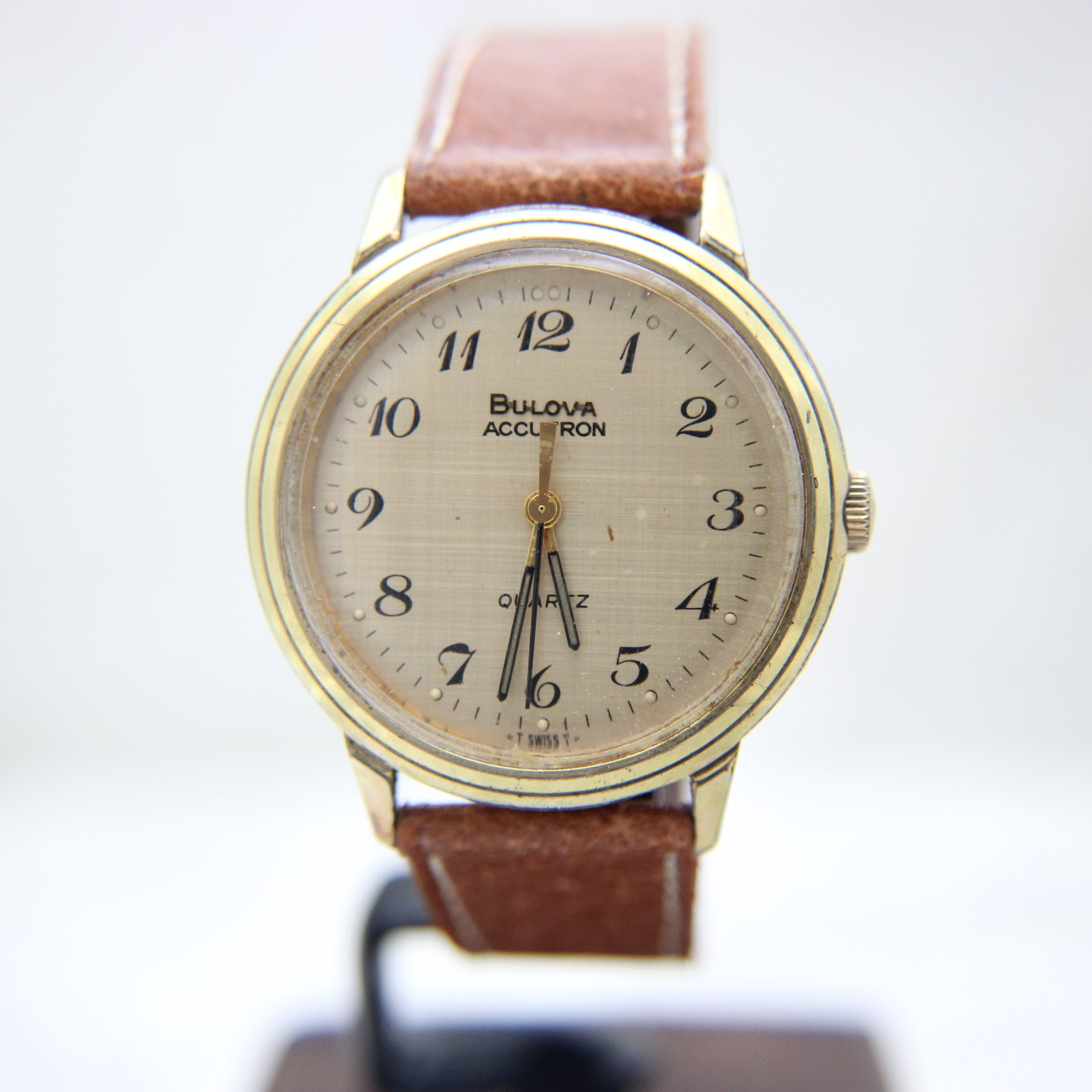 Front view of the Bulova Accutron Quartz watch on a display stand, showing the champagne gold-tone dial with Arabic numerals.