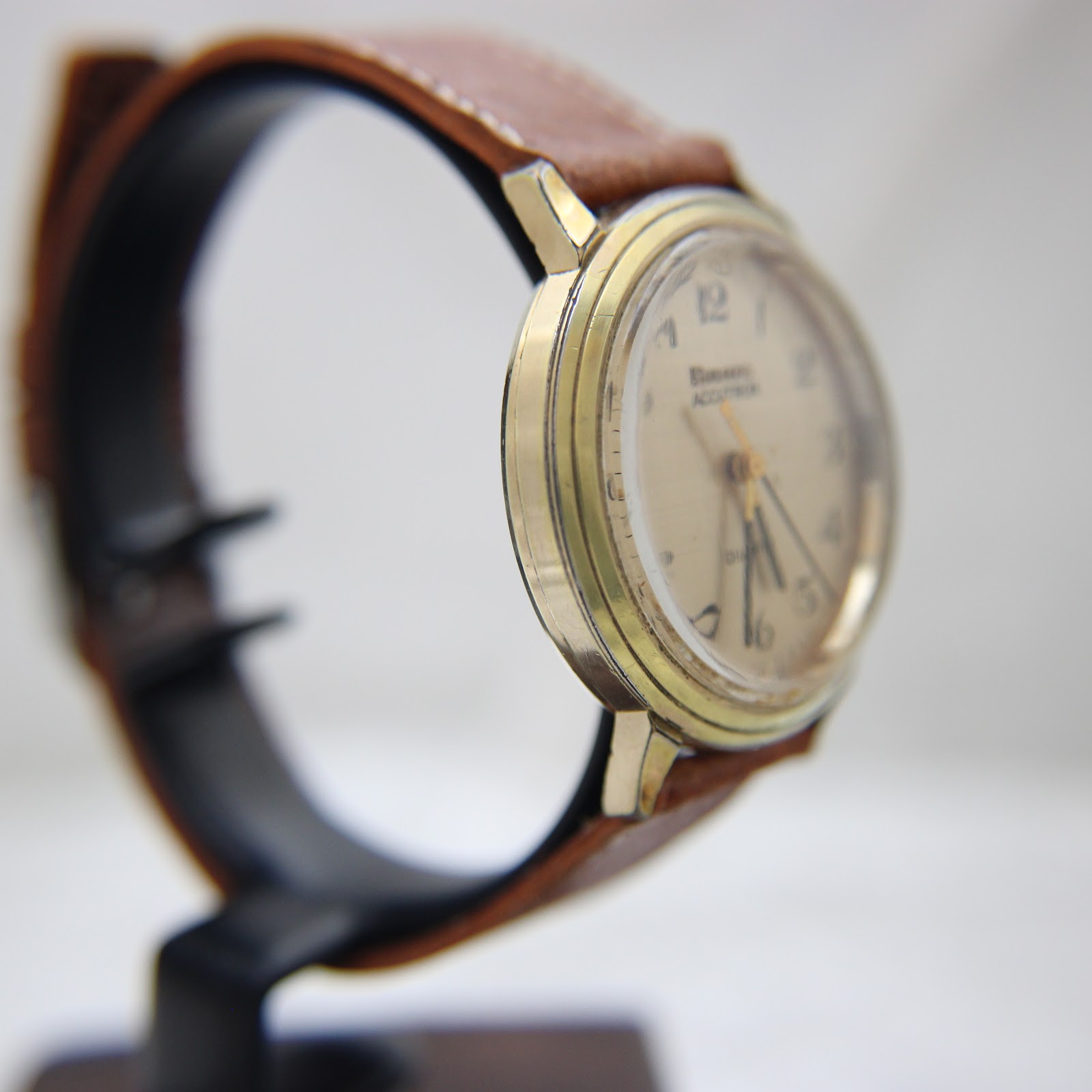 Another side view of the watch on a display stand, highlighting the curved acrylic crystal and case profile.