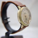 Another side view of the watch on a display stand, highlighting the curved acrylic crystal and case profile.