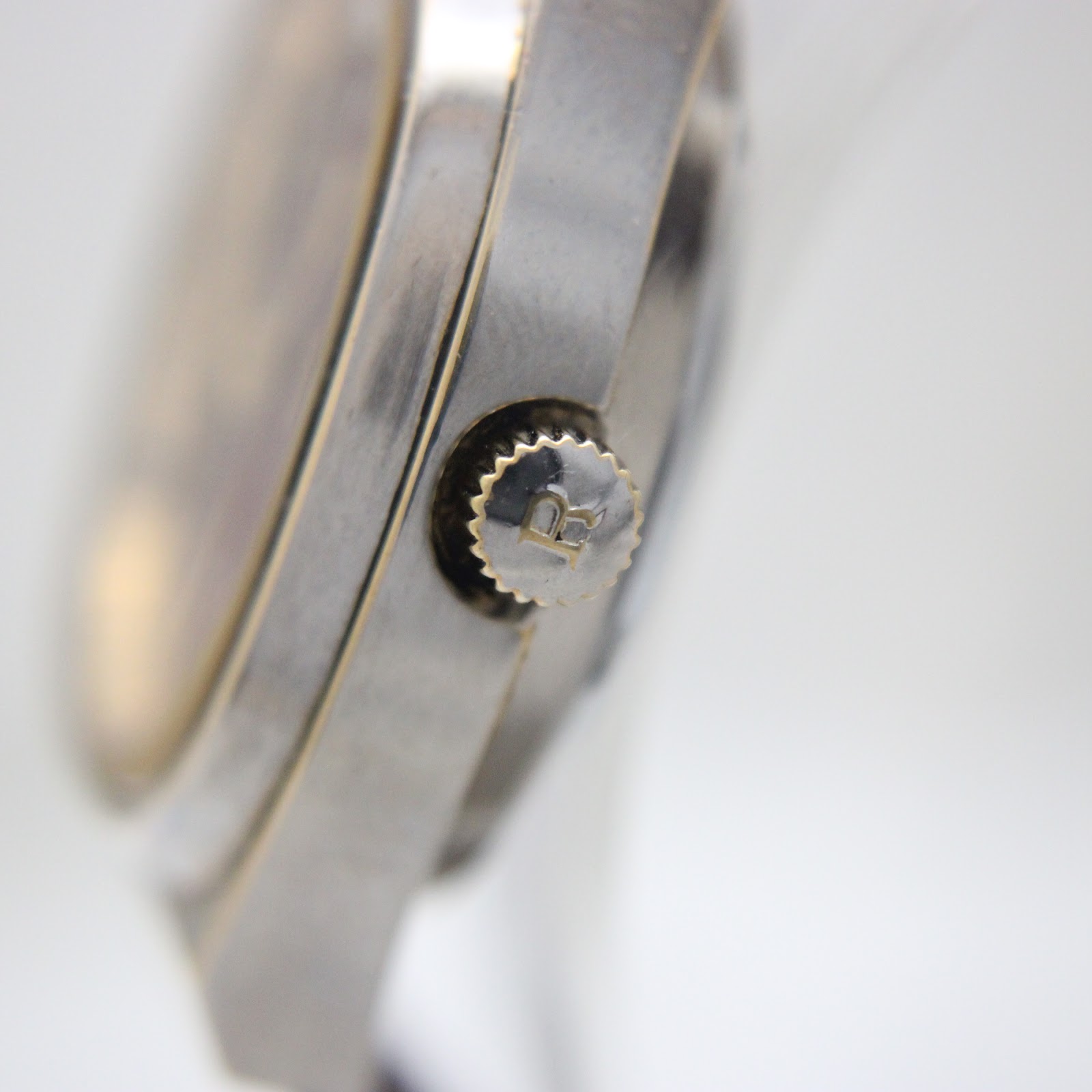 Close-up of the watch crown, detailed with an engraved 'R' logo.