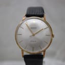 Front view of the Mainstay watch with a silver sunburst dial, gold-plated case, and black leather strap.