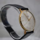 Three-quarter view of the Mainstay watch on a clear stand, highlighting the slim profile and black leather strap.