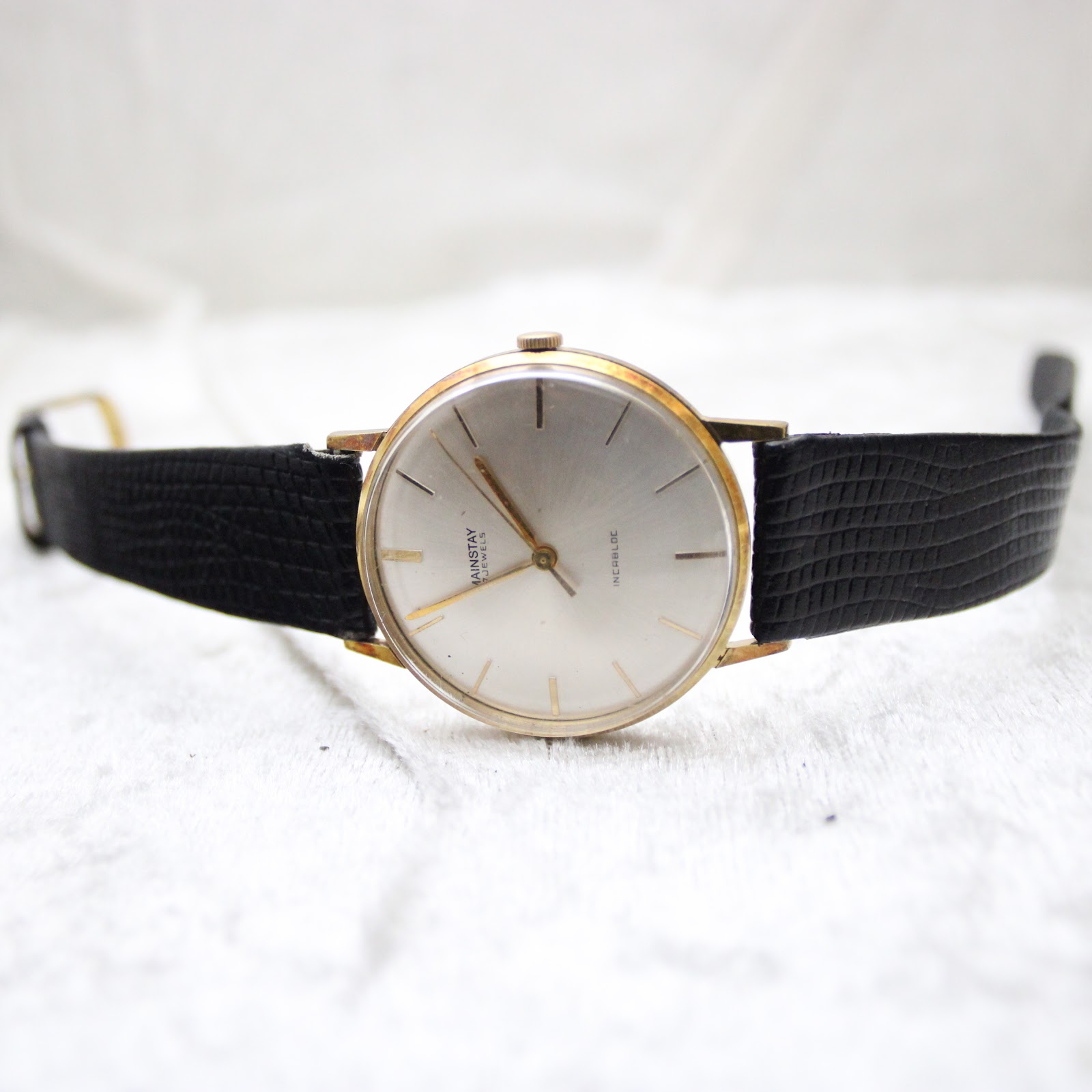 Overhead front view of the Mainstay watch with the black leather strap spread out, dial facing up.