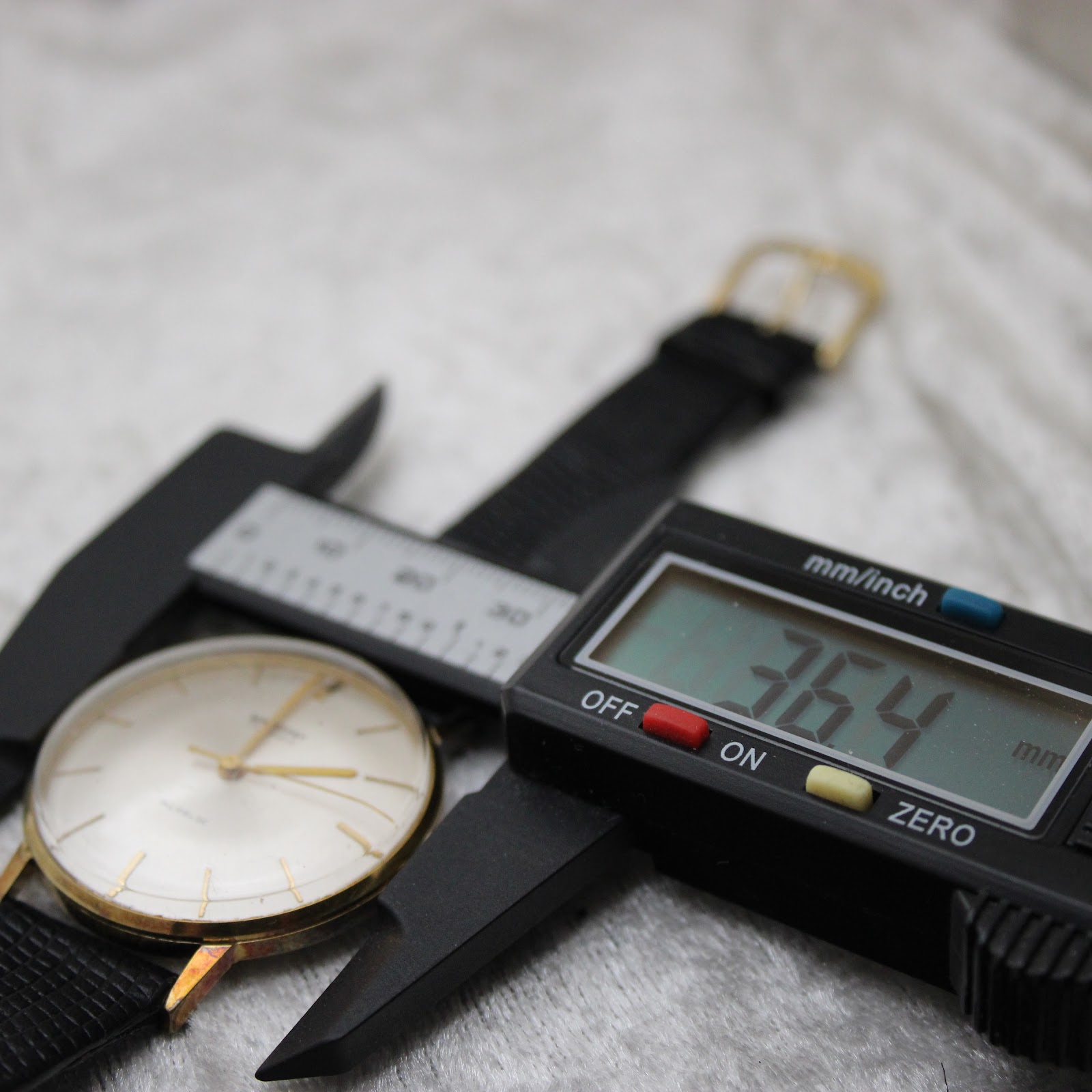 Close-up of a digital caliper measuring the watch width including the crown at 36.4mm.
