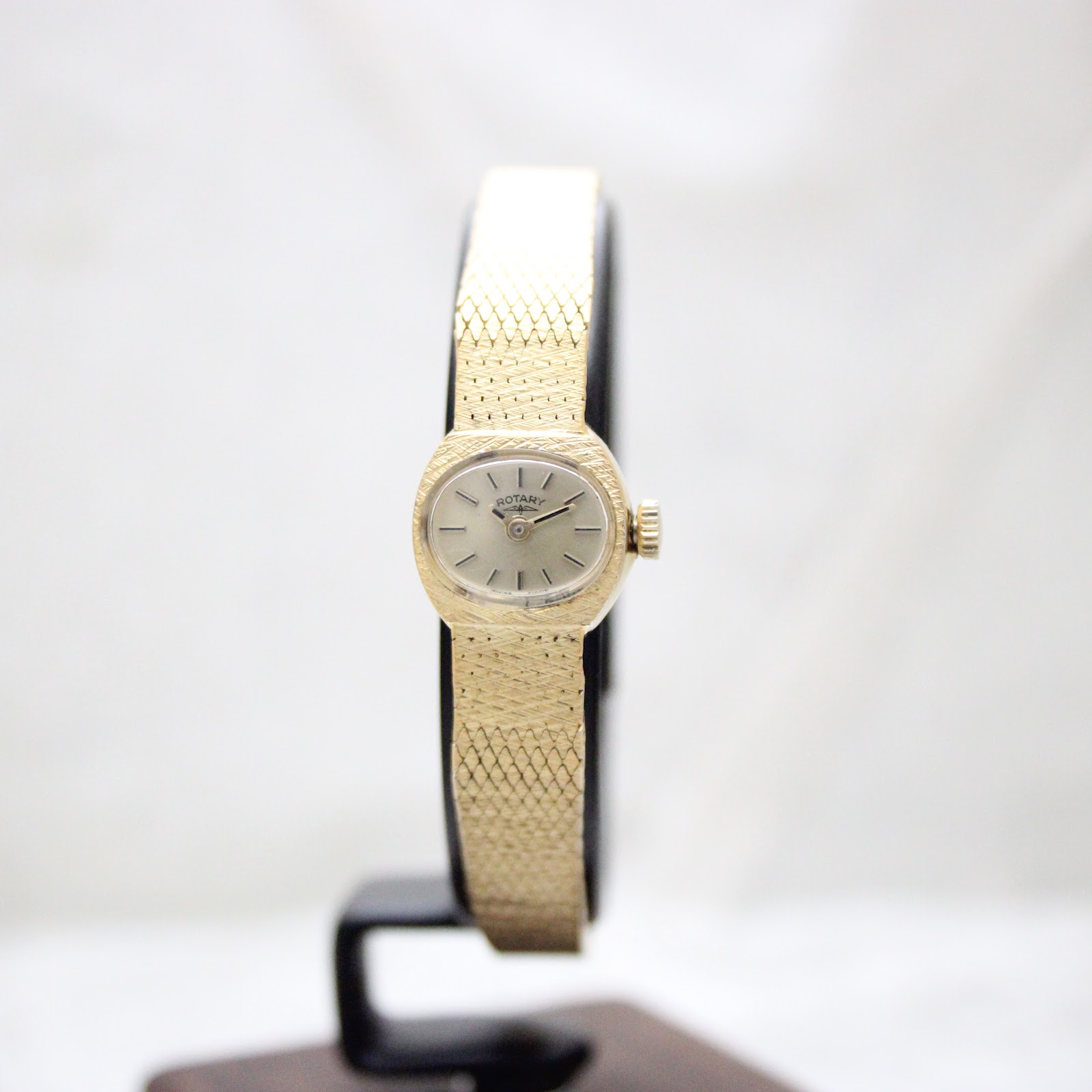 Slightly angled front-left view of the gold-tone Rotary watch on a black stand.