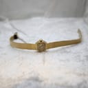 Full length view of the Rotary gold-tone watch with integrated bracelet laid out on a white textured surface.