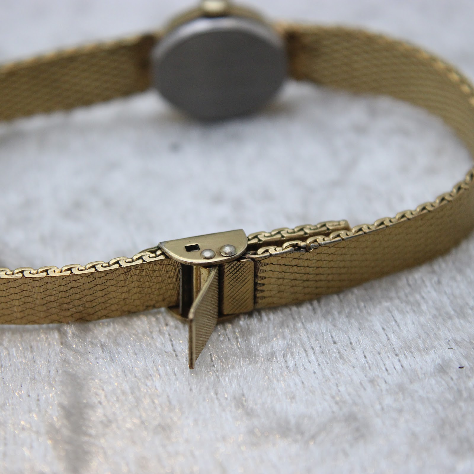 Close-up of the simple fold-over clasp mechanism on the integrated gold-tone bracelet.