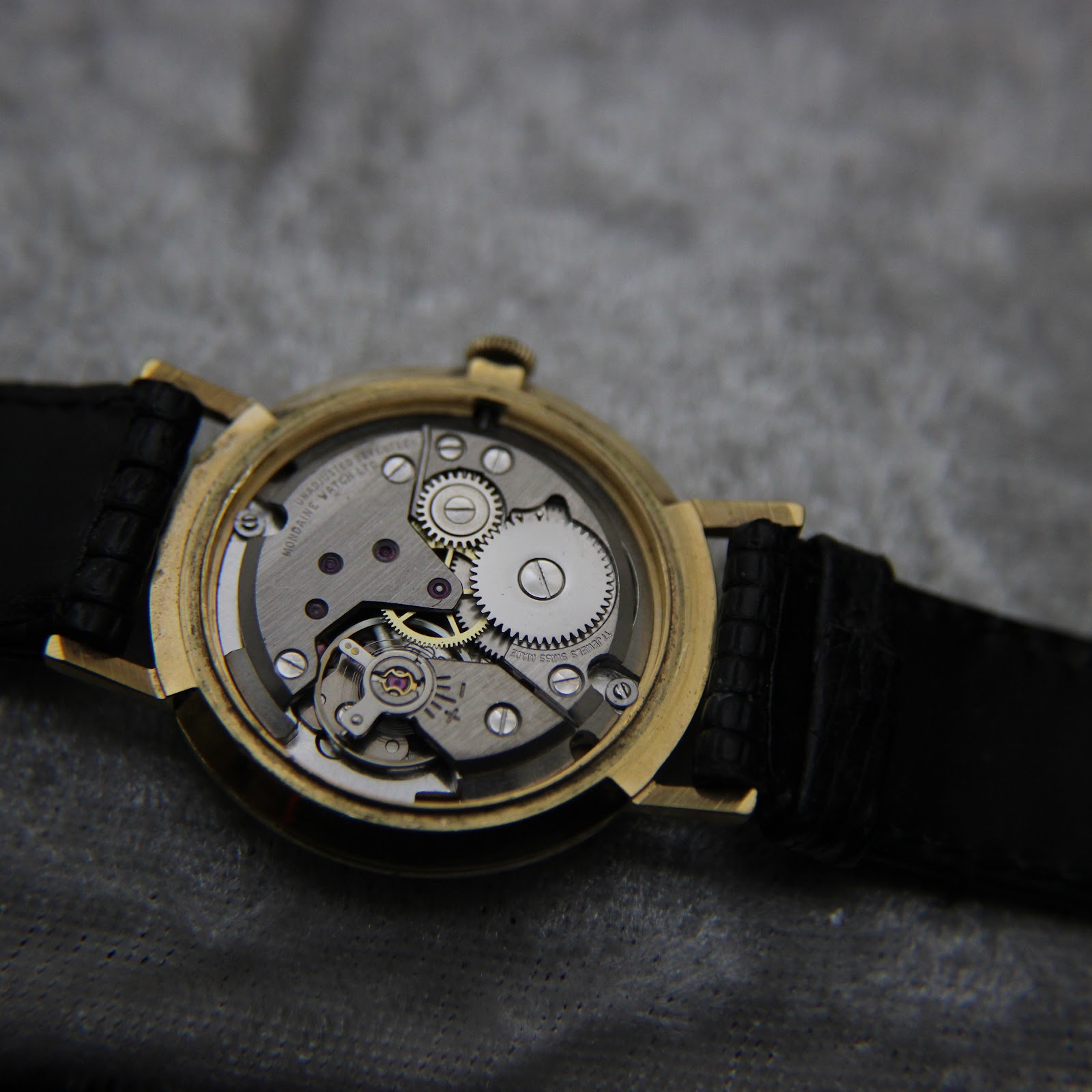 Full view of the open case back, showcasing the entire manual wind movement inside the gold-plated case.