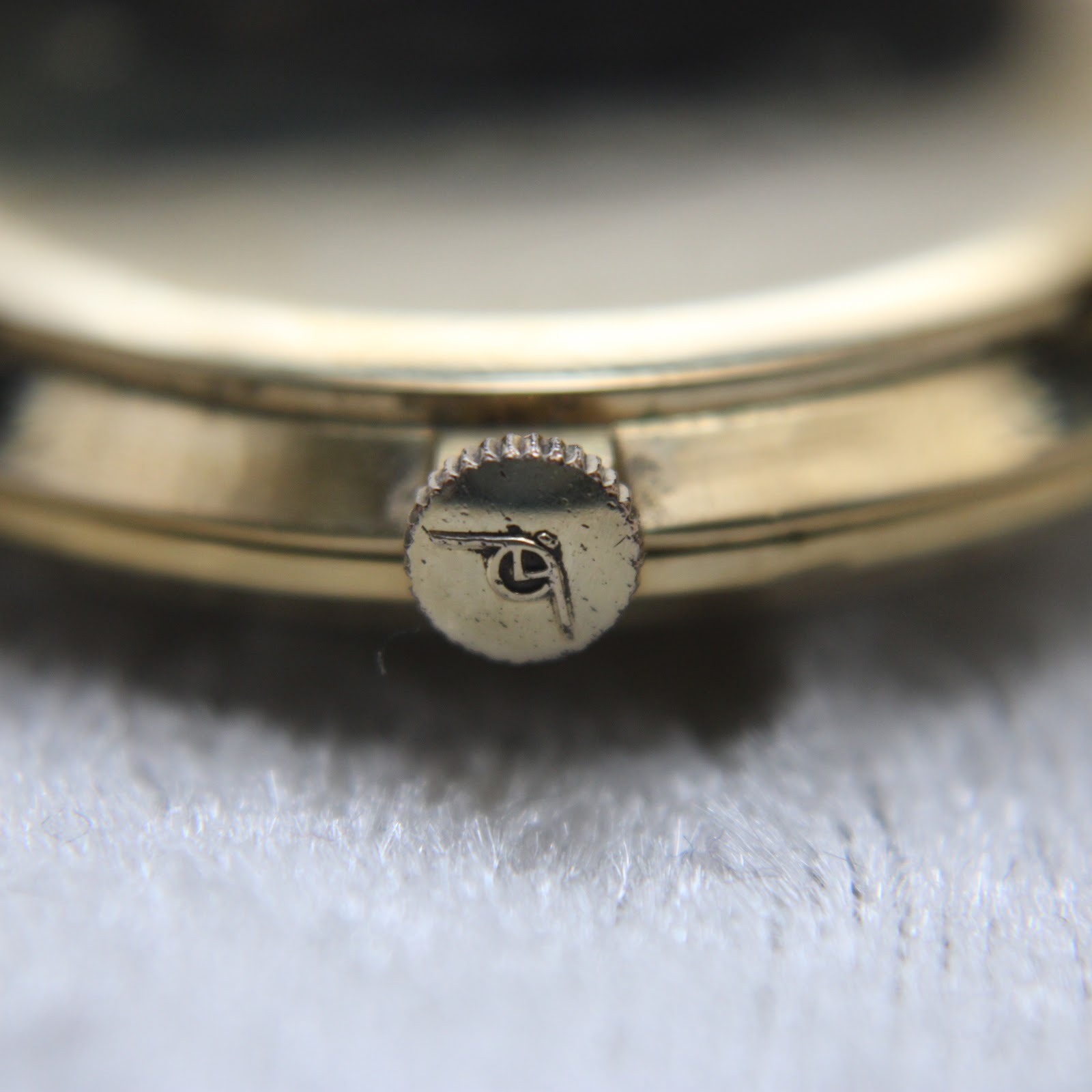 Close-up of the gold-toned crown with the Mondaine 'M' logo.